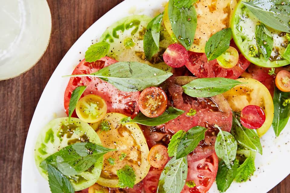 Colorful tomato and herb salad with fresh basil leaves on a white plate