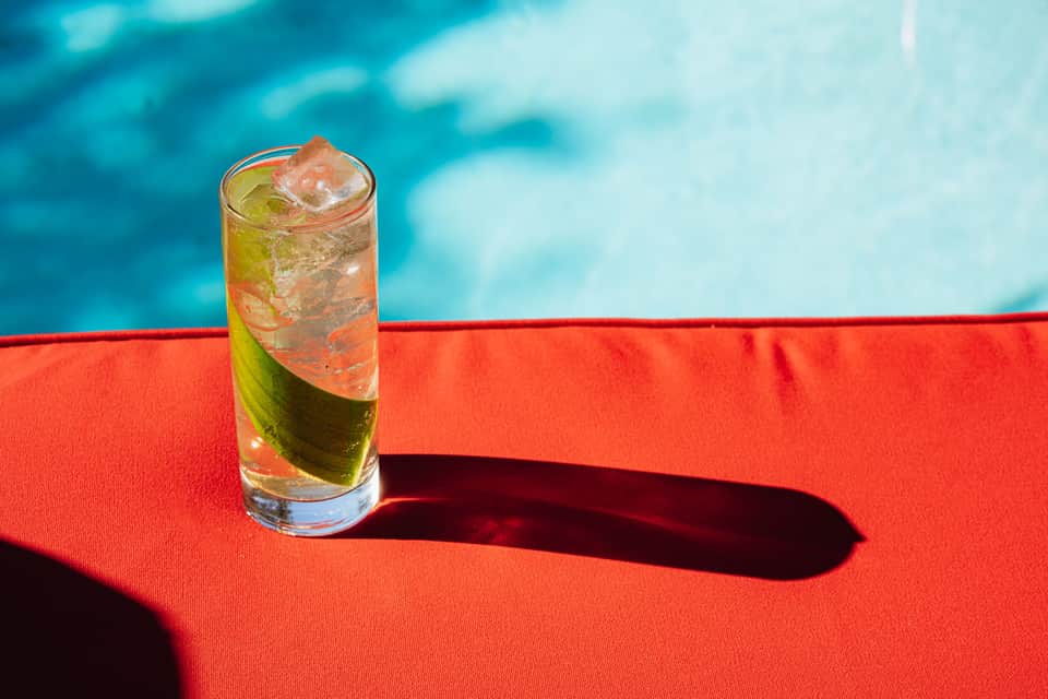 Cocktail with lime and ice on red pool lounger overlooking turquoise water