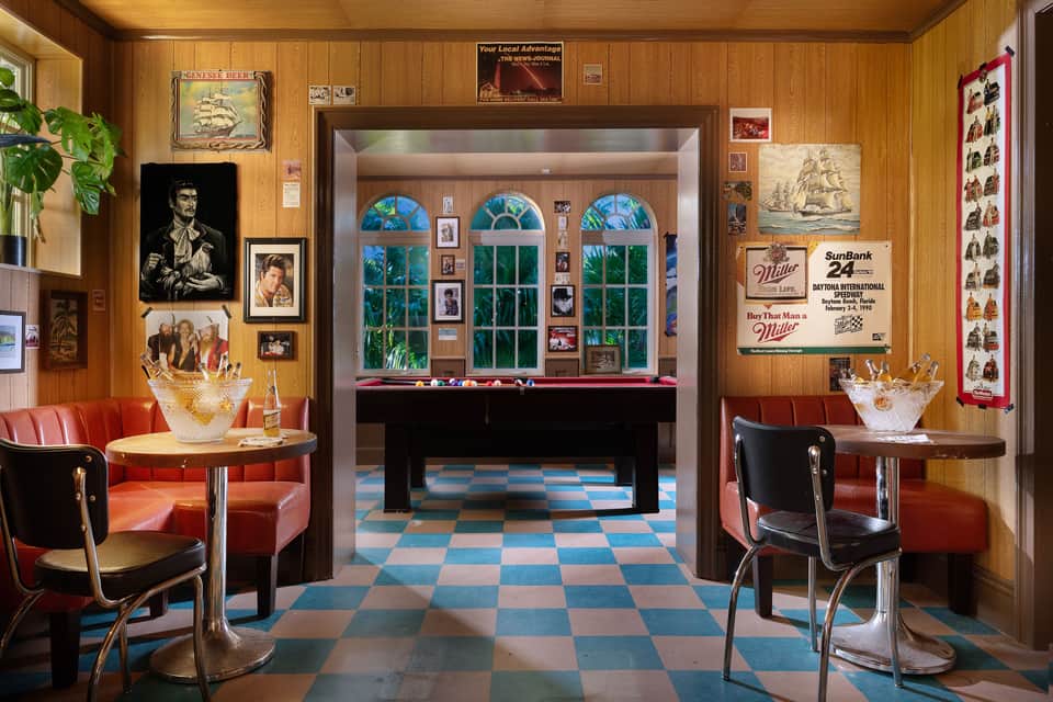 Retro-style recreation room with wood paneling, pool table, red vinyl seating, vintage signage, and checkered floor