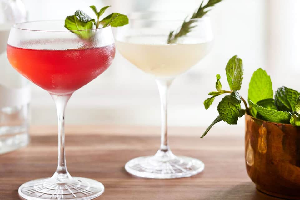 Two colorful cocktails with mint garnish and fresh herbs on a wooden surface