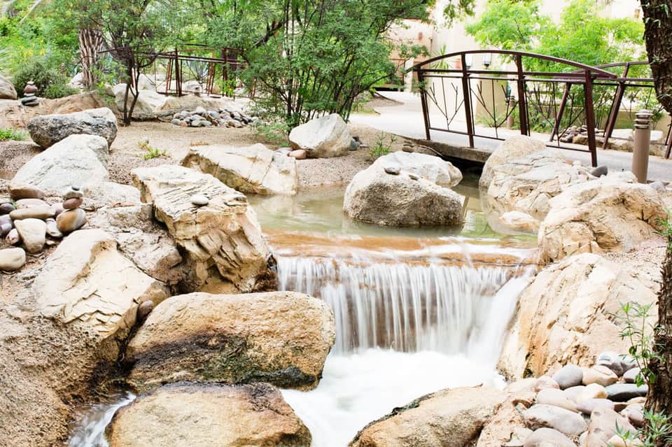 Natural waterfall cascading over rocks in a landscaped garden with wooden bridges and trees