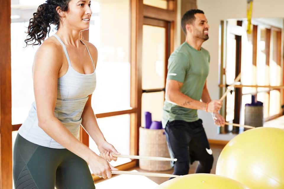 Two people exercising indoors with battle ropes and gym equipment