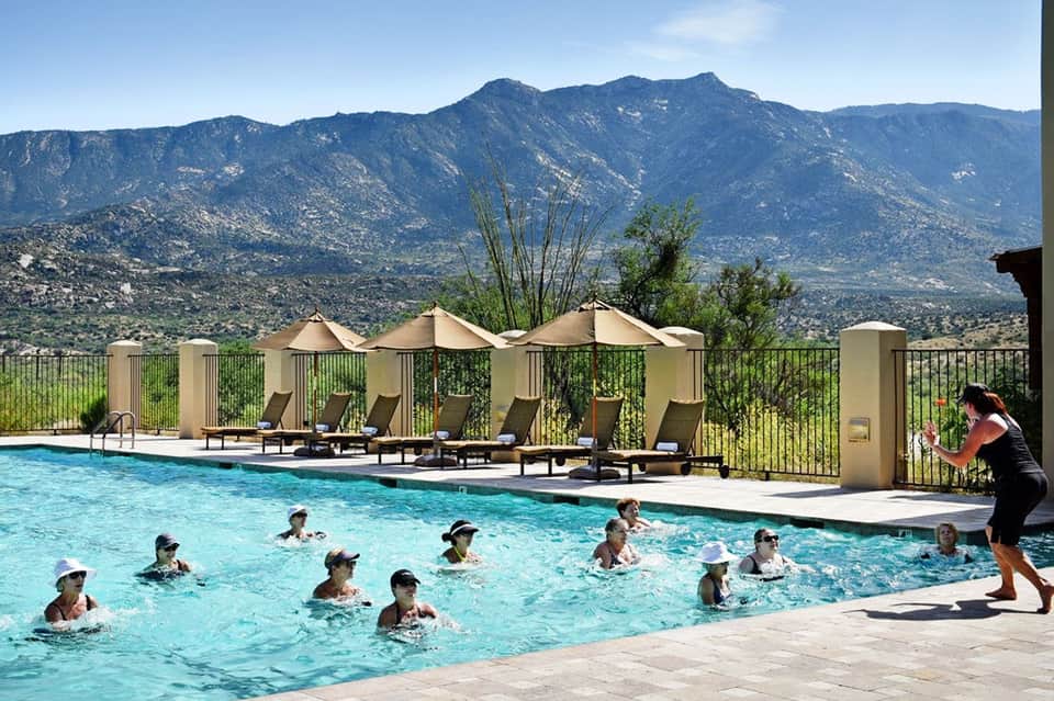 Resort pool with guests swimming, mountain views, lounge chairs, and cream umbrellas