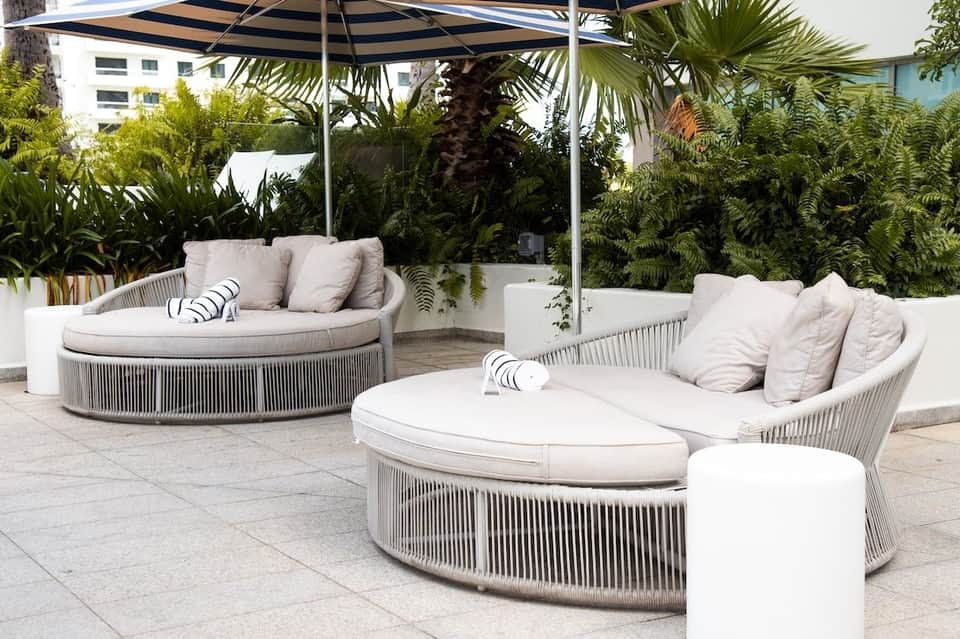 Modern lounge seating area with round white cushioned chairs, black and white umbrellas, and tropical plants