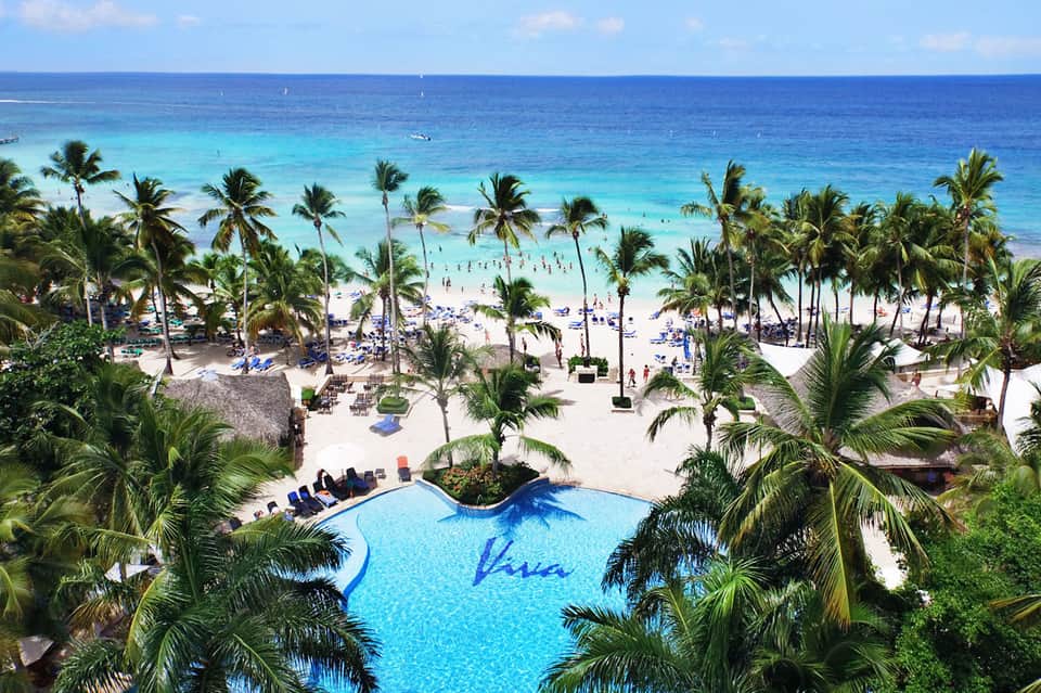 Tropical beach resort with curved pool, palm trees, and ocean view with sunbathers