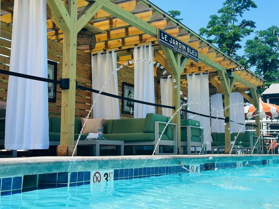 Poolside lounge area with green pergola, white curtains, green seating, and turquoise swimming pool
