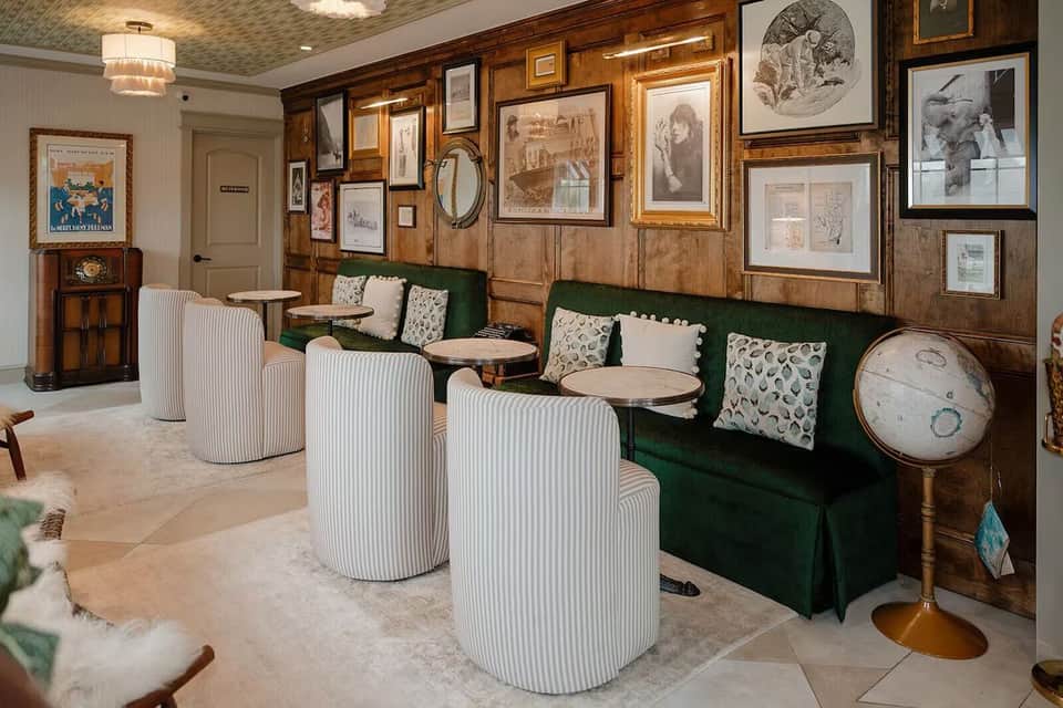 Vintage-inspired lounge with wood paneling, green velvet benches, striped armchairs, and eclectic framed artwork