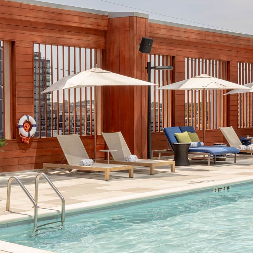 Pool deck with loungers under umbrellas, wooden privacy screens, and city skyline view