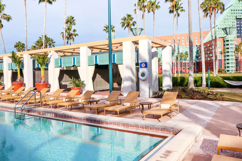 Modern poolside cabanas with white columns and tan lounge chairs beside bright turquoise pool