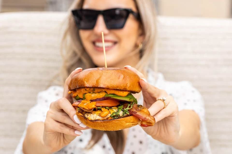 Woman holding a gourmet burger with multiple layers and fresh toppings