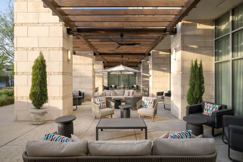 Outdoor patio with wooden pergola, stone columns, cream lounge seating, striped pillows, and potted greenery