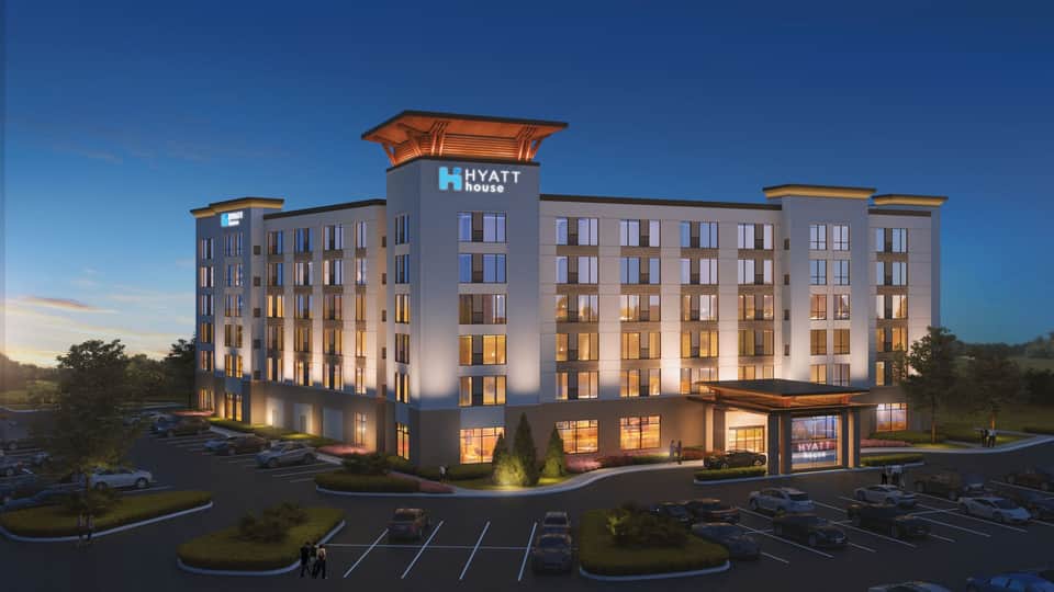Hyatt House hotel exterior at dusk with illuminated facade, parking lot, and landscaping under clear blue sky