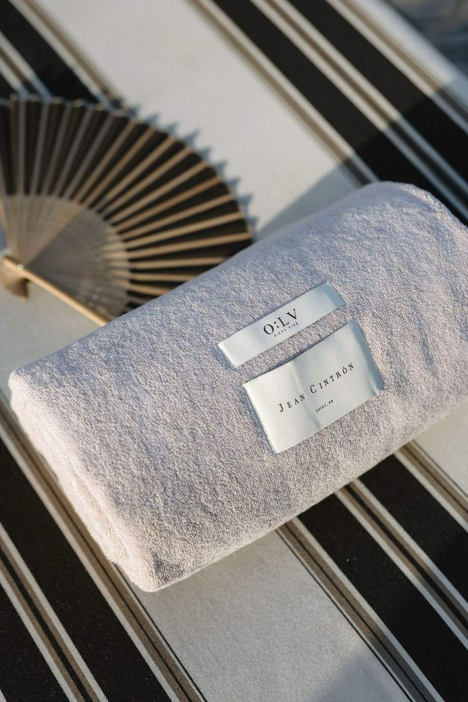 Folded gray towel with OILY and Jean Cintron labels on striped lounge chair