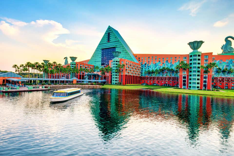 Colorful waterfront resort with turquoise pyramid roof, orange and blue buildings reflected in water