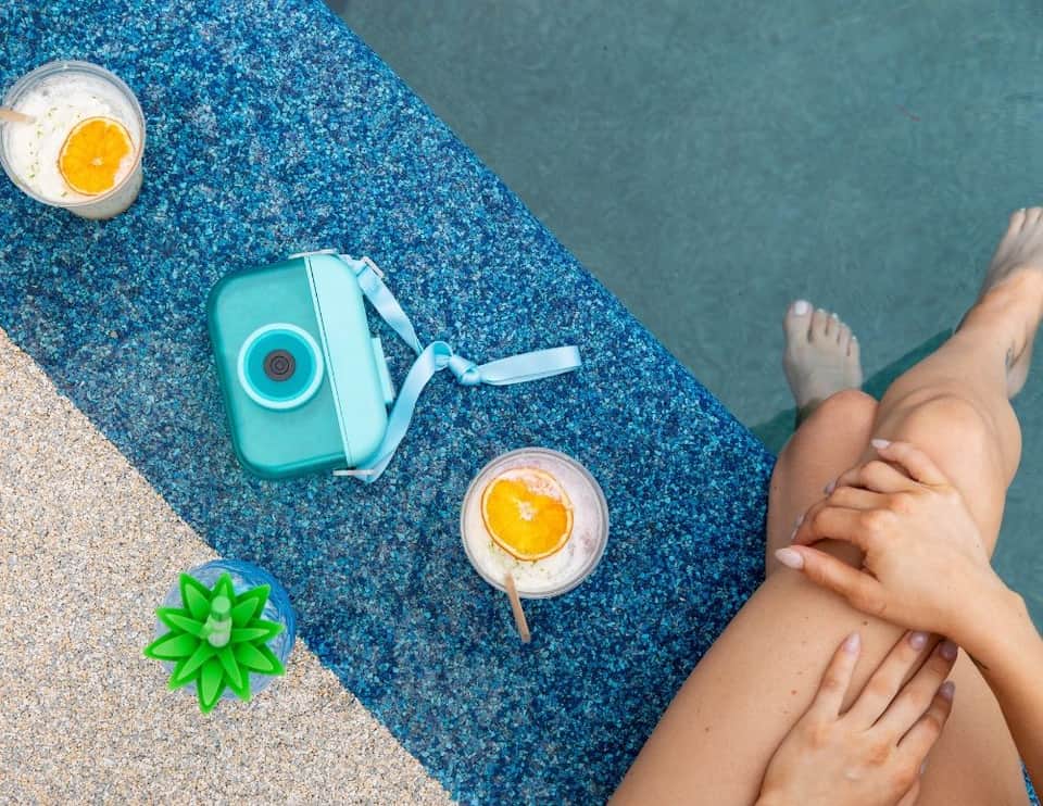 Overhead view of poolside drinks and a turquoise camera on a blue textured pool lounger