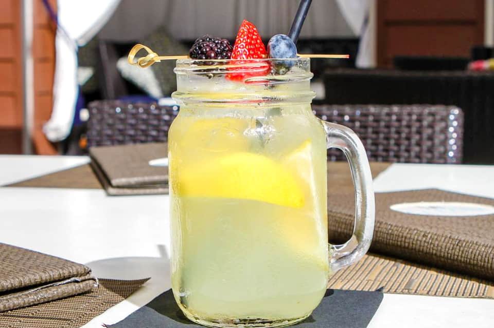 Tropical cocktail in mason jar with fresh berries and citrus garnish on table