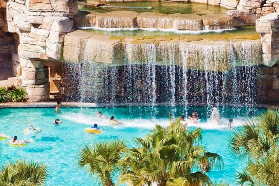 Turquoise spring-fed pool with cascading waterfall and stone structures, guests swimming and relaxing on floats