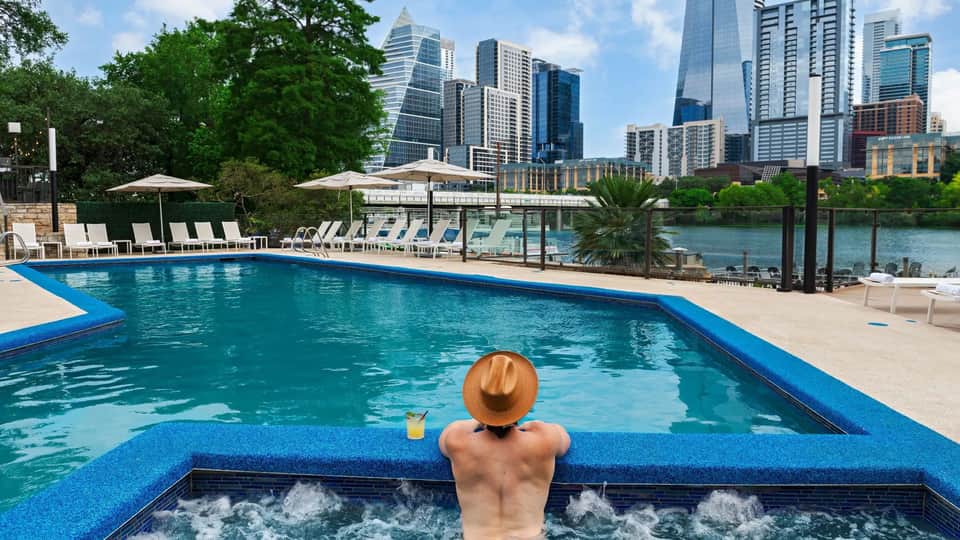 Guest relaxing in hot tub overlooking resort pool and city skyline with river view