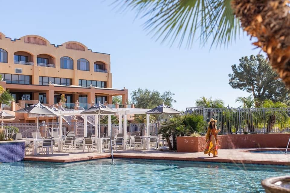 Resort pool area with white umbrellas, loungers, and Mediterranean-style building