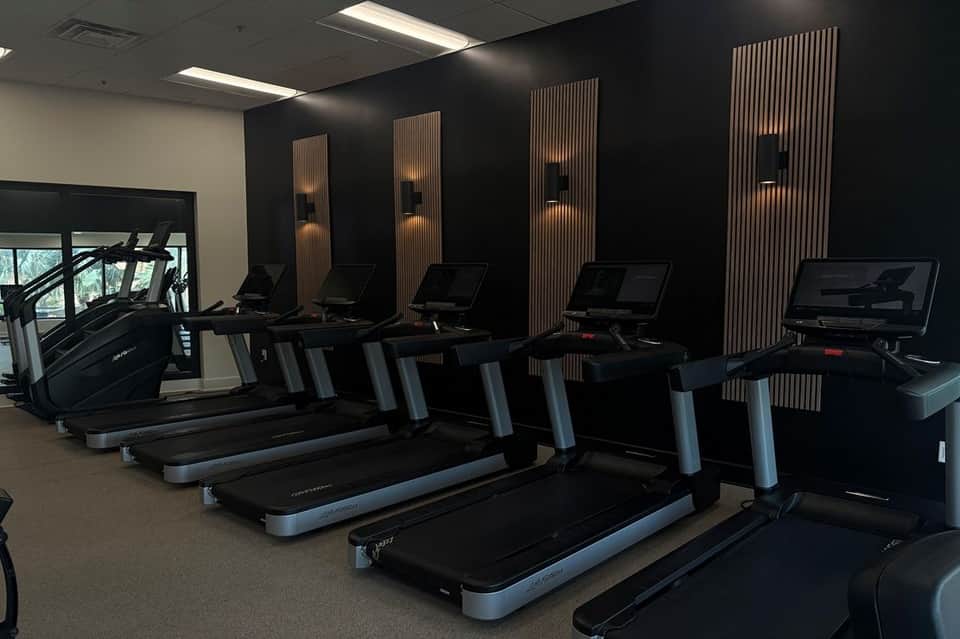 Modern fitness center with black treadmills, wooden accent walls, and studio lighting