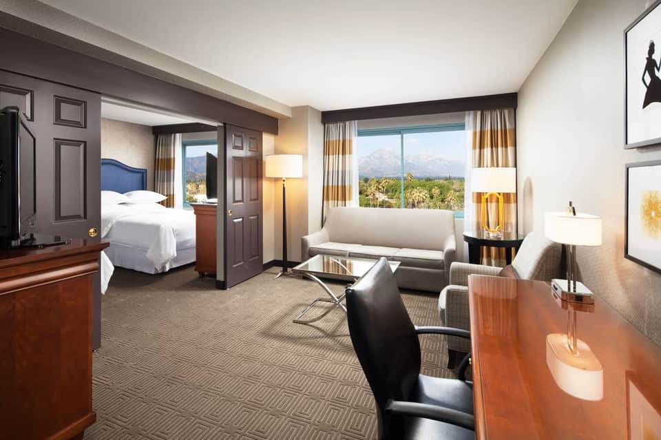 Luxury hotel room with mountain view, separate living area with sofa, and blue-upholstered bed