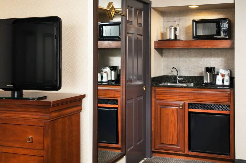 Hotel suite kitchenette with wood cabinetry, black appliances, and dark countertops