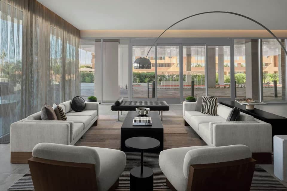 Modern living room with white sectional seating, floor-to-ceiling windows, and city views