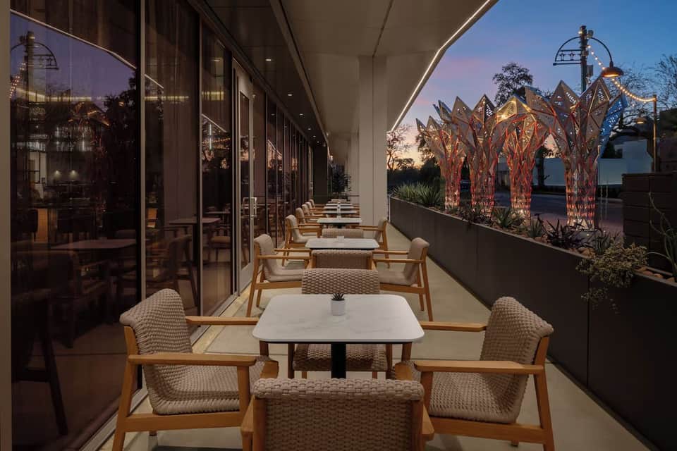 Modern terrace with wooden chairs, white tables, glass railings, and illuminated sculptural trees