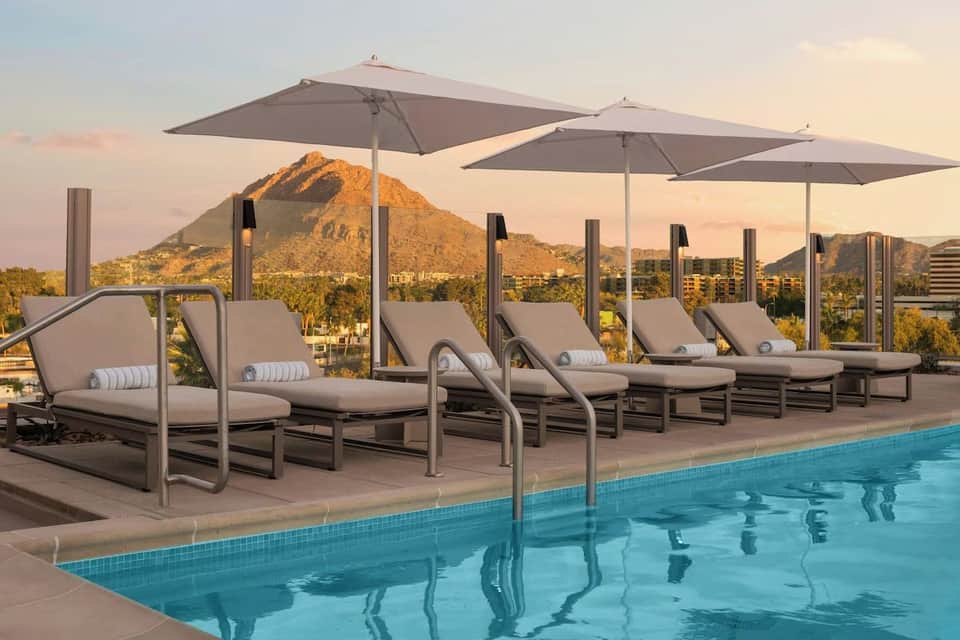Rooftop pool with lounge chairs and umbrellas overlooking a desert mountain at sunset