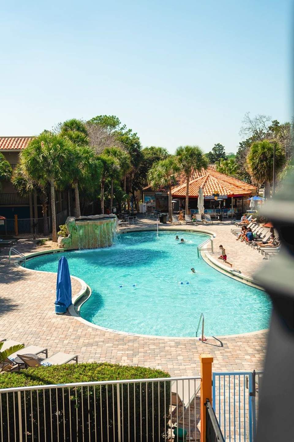 Tropical resort pool with turquoise water, palm trees, tiki-roof buildings, and lounge chairs on sunny day