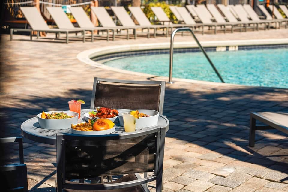 Poolside table with food and beverages, lounge chairs, and resort amenities in background