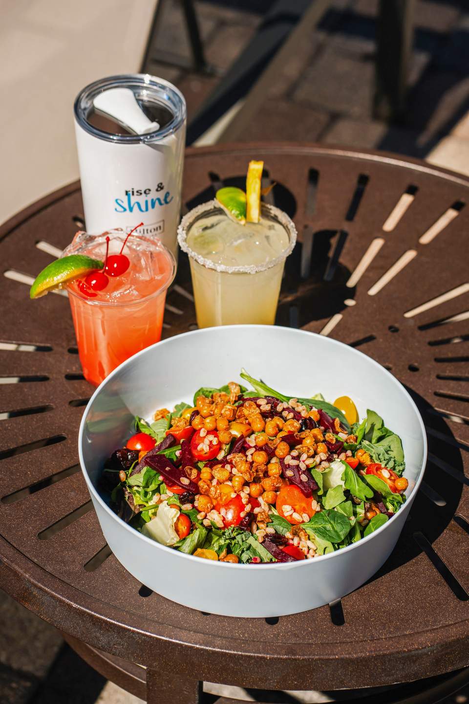 Colorful salad bowl with chickpeas and vegetables, served with cocktails on a poolside table