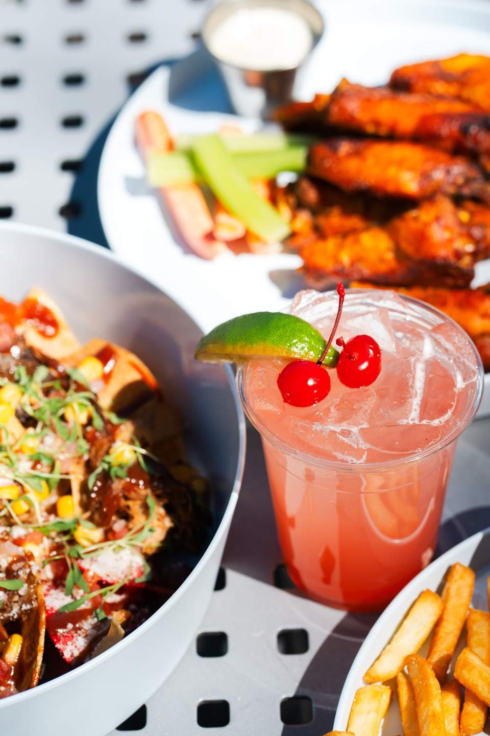Spicy tacos and pink cocktail with cherries, served with wings and fries poolside