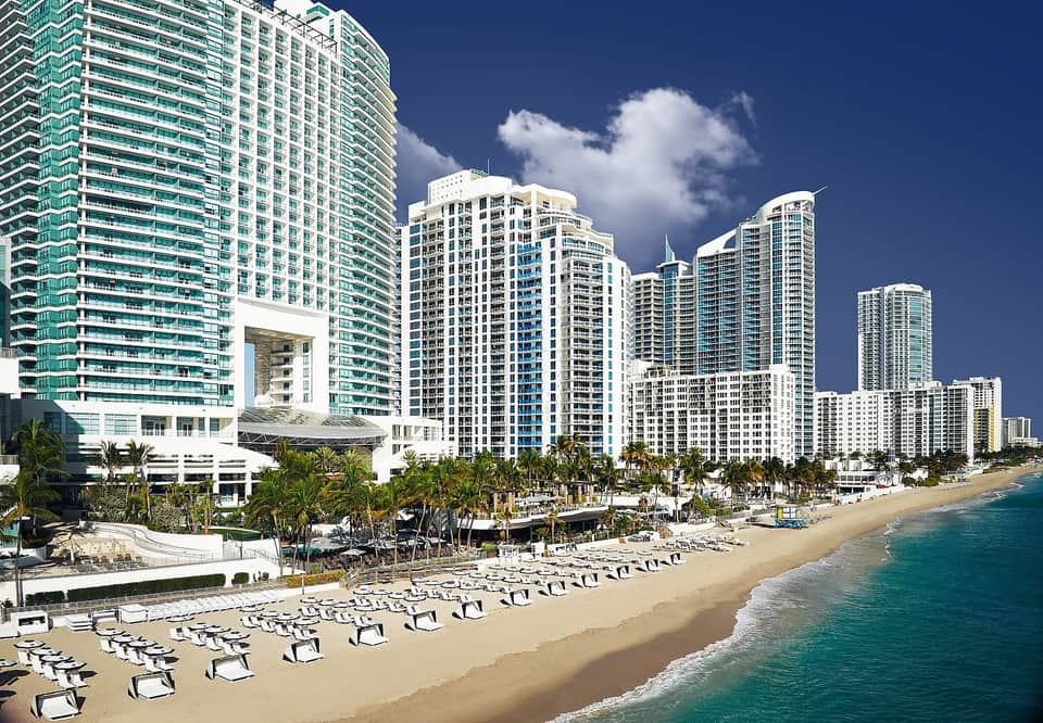 High-rise beachfront hotels with white and turquoise balconies, sandy beach, and ocean waves
