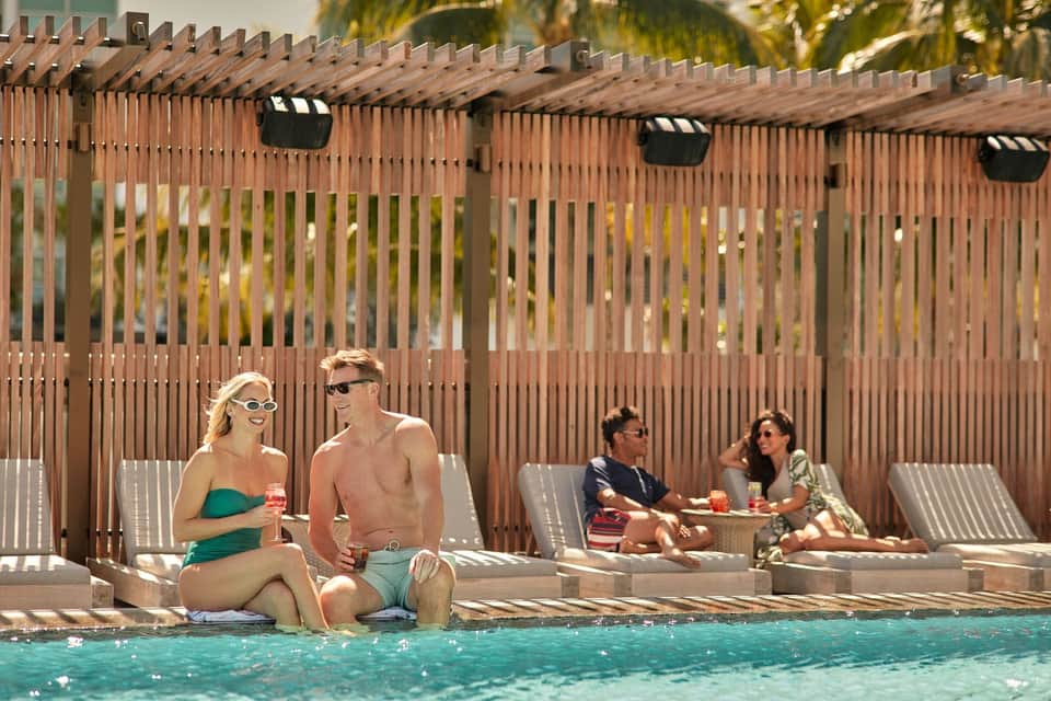 Pool area with wooden pergola shade structures, guests lounging poolside on sunny day