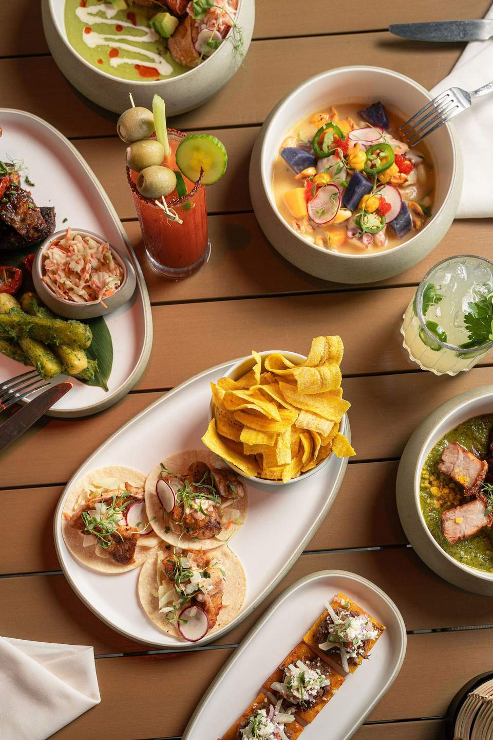 Overhead view of gourmet meal with tacos, soup, beverages, fries, and seafood dishes on wooden table