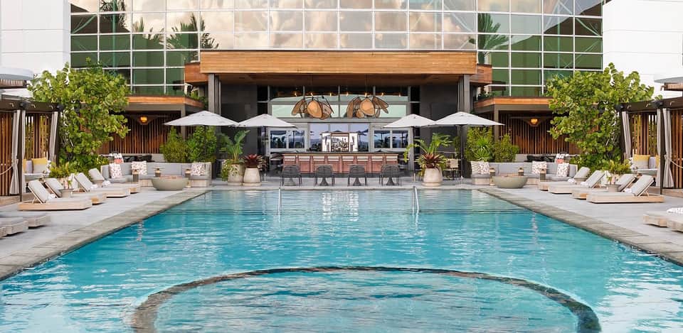 Modern resort pool with bar, white lounge chairs, umbrellas, and contemporary architecture