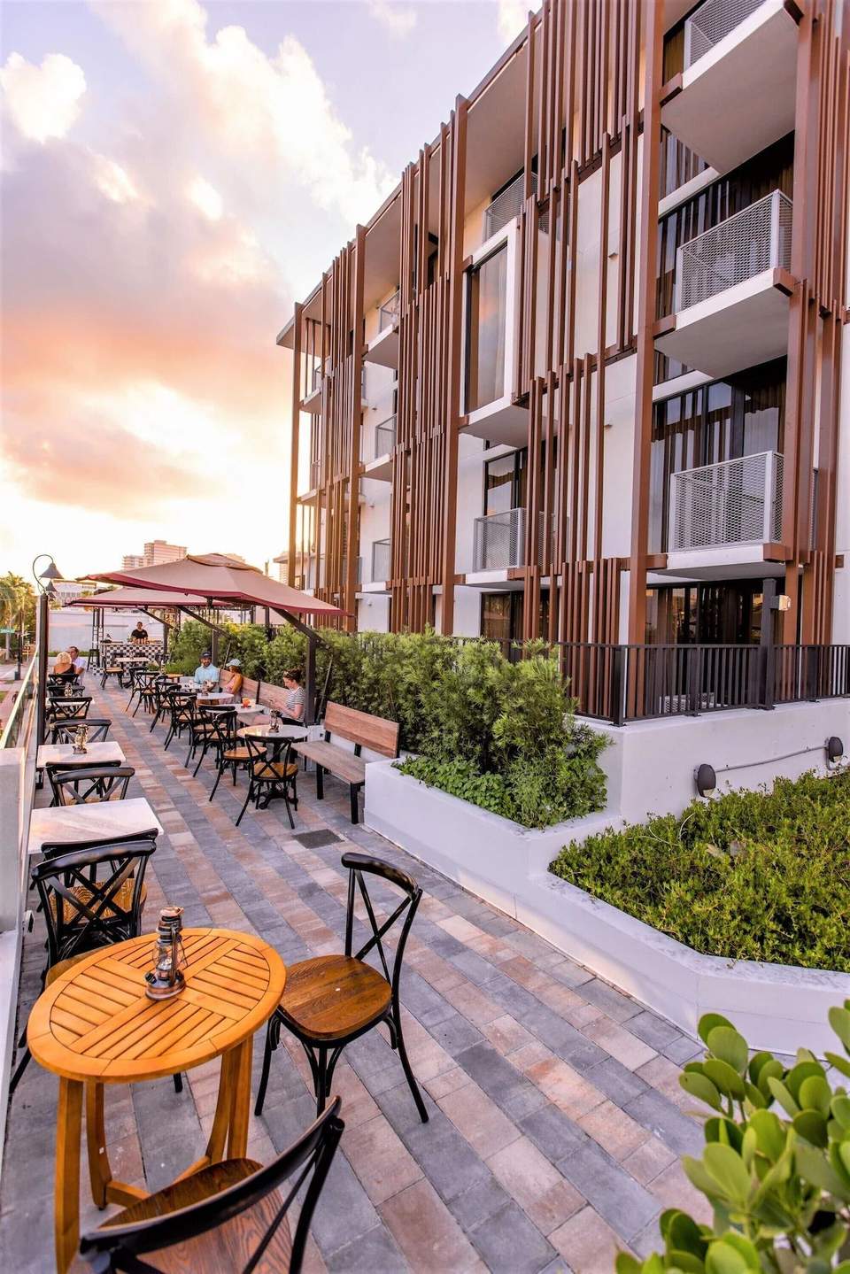 Outdoor courtyard seating area at dusk with umbrellas, wooden tables, modern building facade, and landscaping