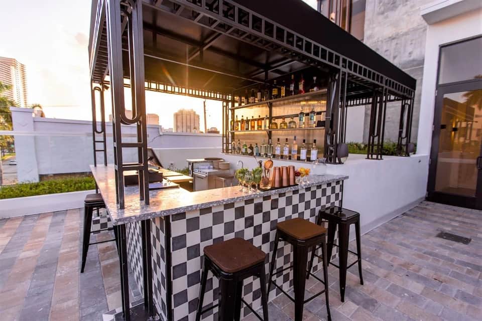Modern rooftop bar with black and white checkered counter, bottle display, and sunset views