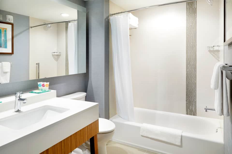 Modern bathroom with gray tile walls, white vanity, large mirror, bathtub, and shower enclosure