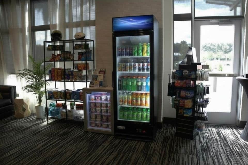 Hotel lobby area with beverage coolers, snack display, shelving with merchandise, and large windows