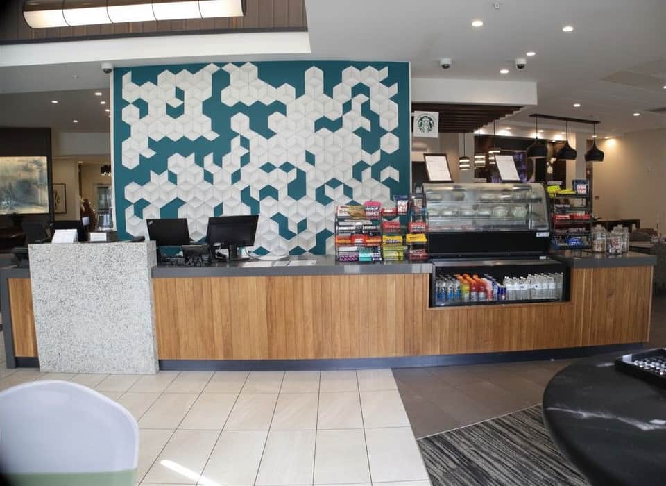 Modern hotel lobby desk with geometric teal and white wall art, wooden cabinetry, and service counter