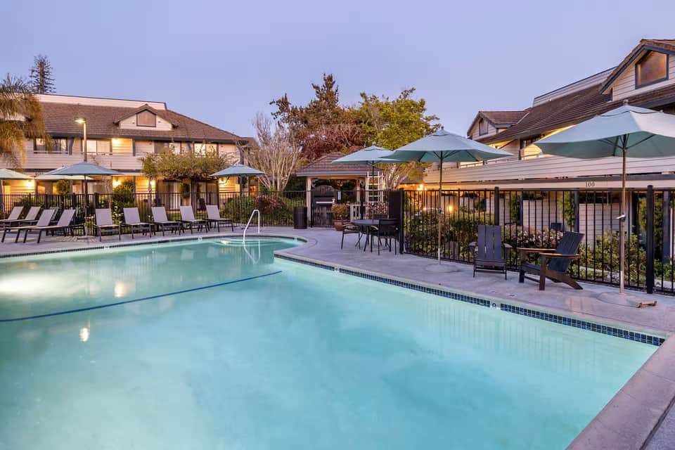 Resort swimming pools with lounge chairs and green umbrellas at dusk