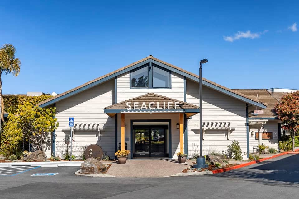 Seacliff resort entrance with white siding, yellow awning, and landscaping