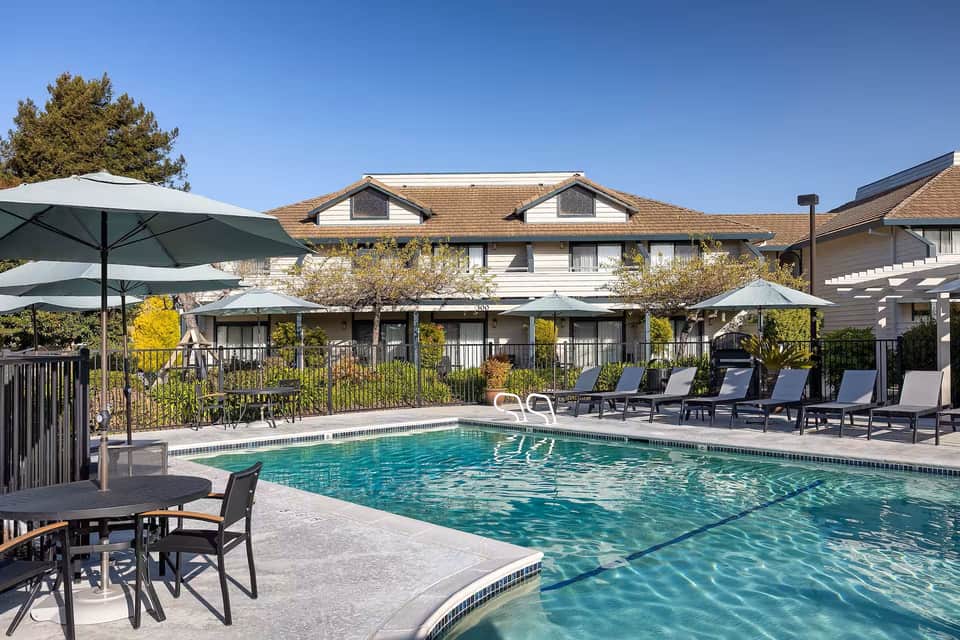 Rectangular swimming pool with lane markings, patio seating area, and multi-story residential buildings behind