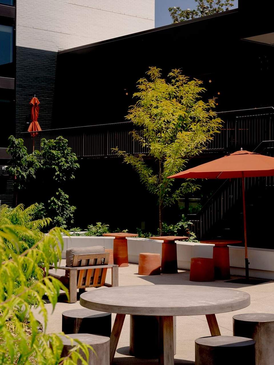 Modern courtyard with round concrete tables, terracotta seating, black walls, and orange umbrella