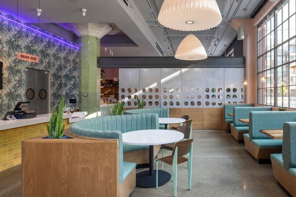 Contemporary cafe interior with turquoise booths, pendant lights, and open kitchen display
