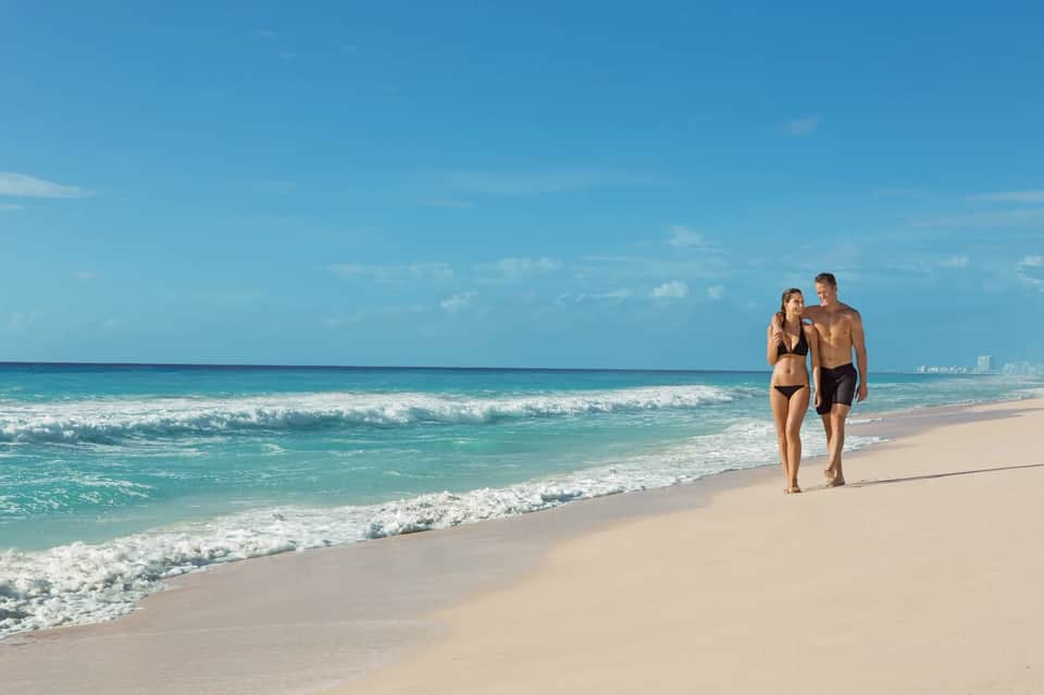 Couple walking along sandy beach with turquoise ocean waves and blue sky