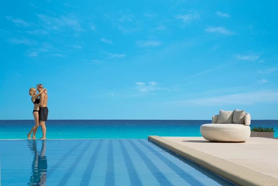 Couple in infinity pool overlooking ocean with modern seating pod on deck