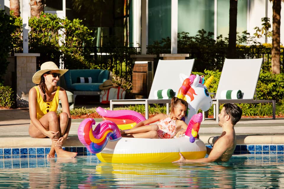 Family enjoying colorful pool floats in resort swimming pool with modern loungers nearby